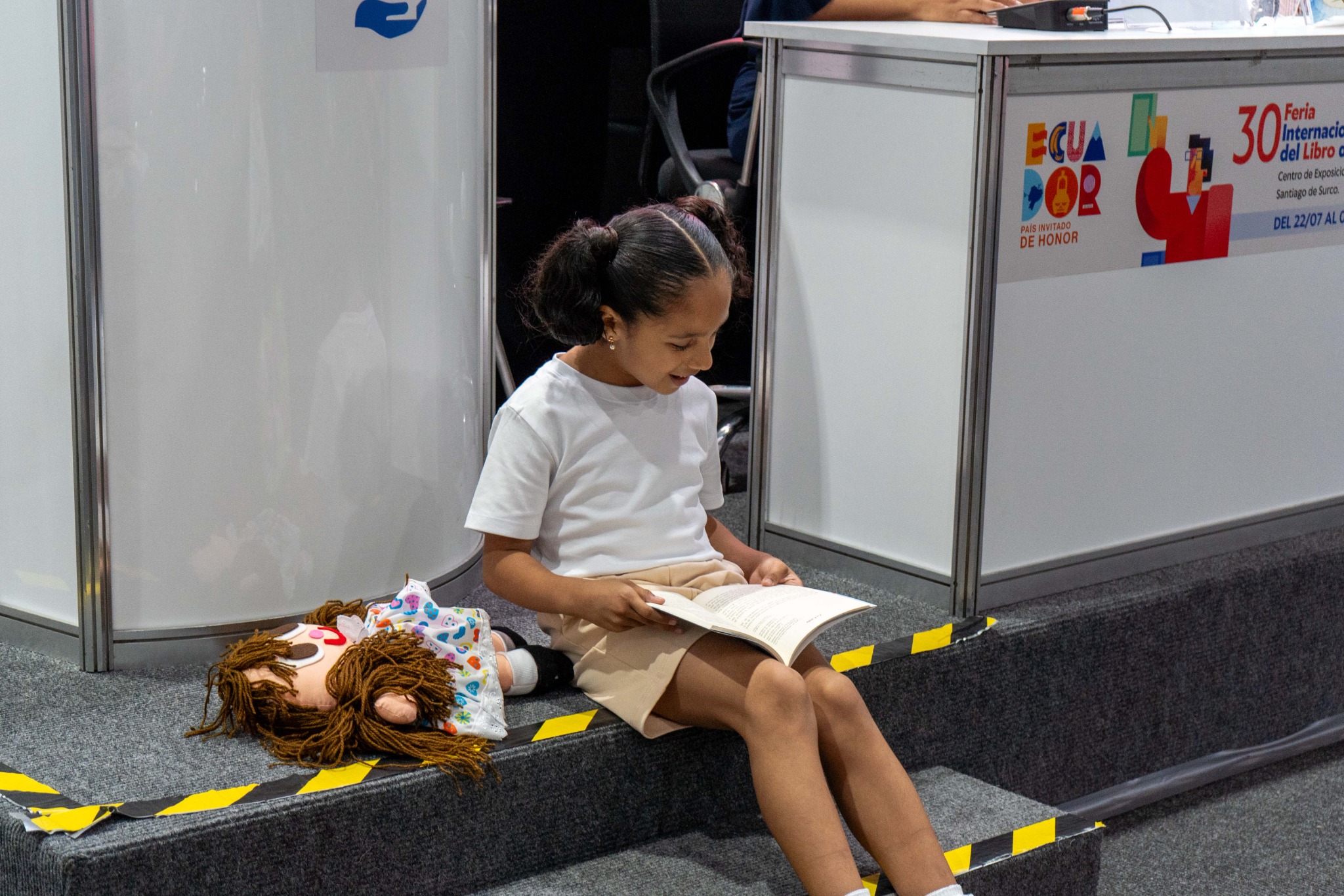 La niña protagonista lee el libro junto a la muñeca de trapo